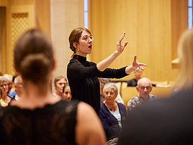 junge Dirigentin vor Orchester stehend