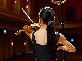 Junge Musikerin von hinten auf der Bühne mit Instrument