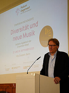 Redner Olaf Wegener vor Rednerpult im Hintergrund eine Leinwand mit Text, Podium Gegenwart, Deutscher Musikrat