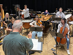 musizierende Menschen mit Instrumenten, Orchester, probend vor dunklem Vorhang