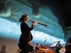 Frau Blasinstrument spielend auf einer Bühne mit Orchester