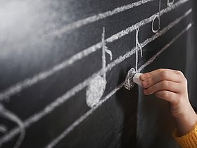 Kind schreibt Musiknoten an Tafel